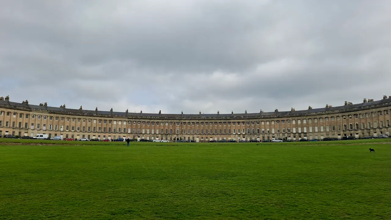 The long curve of the Royal Crescent in Bath seen across its wide green lawn under a grey sky