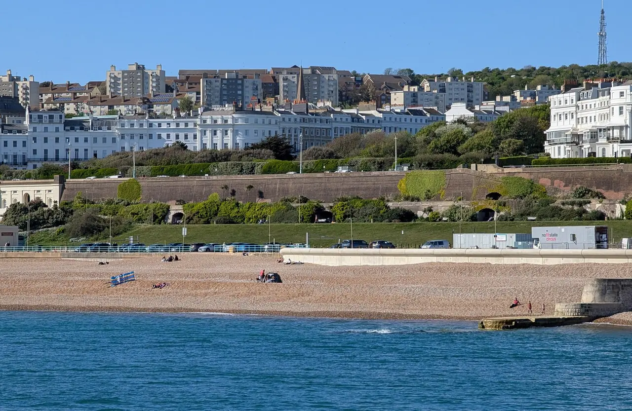 A shingle beach at Black Rock under a blue sky, with the white Regency terraces of Kemp Town on the hill behind and the sea in front