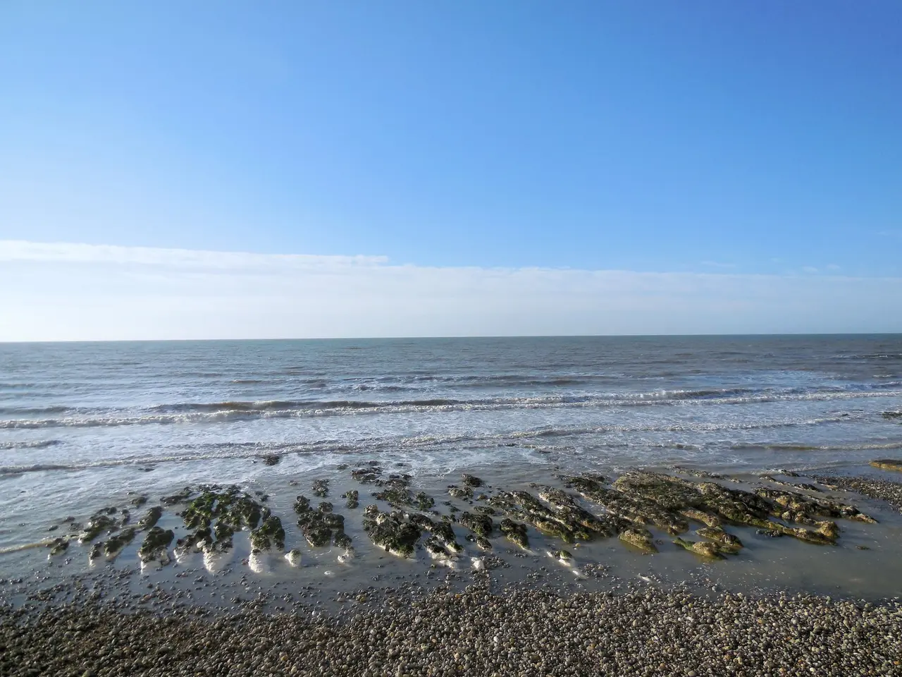 Low tide at Rottingdean, with chalk rocks showing at the water's edge below a clear blue sky