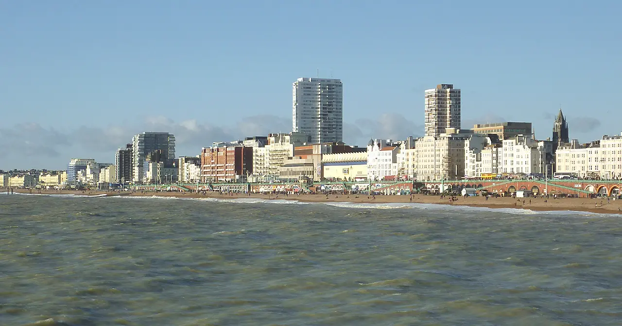 Brighton's seafront seen from the sea, with white and cream hotels and tall blocks behind the beach under a blue sky