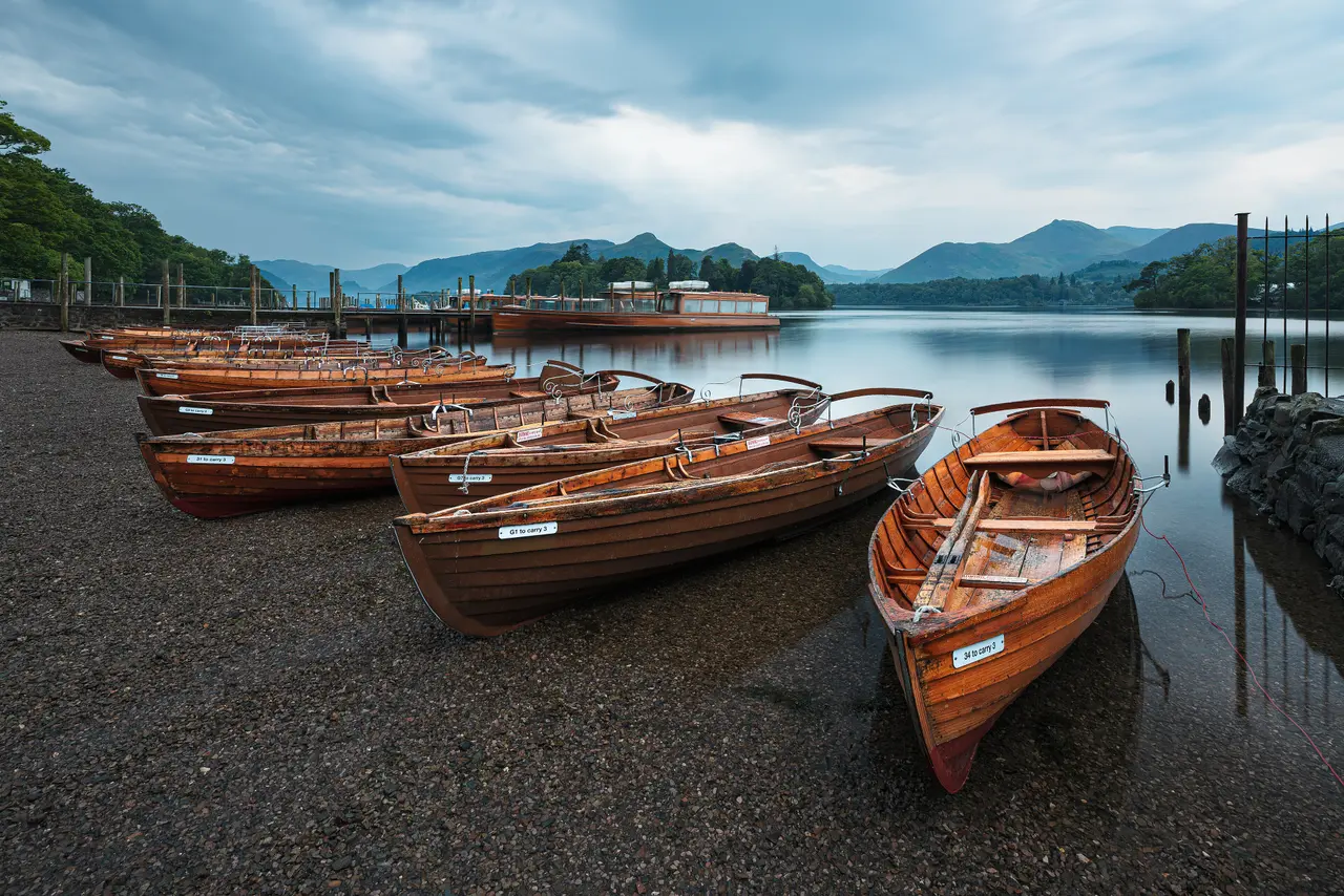 Wooden rowing boats pulled up on the shingle at the Keswick landing stages, with Derwent Water and the fells behind