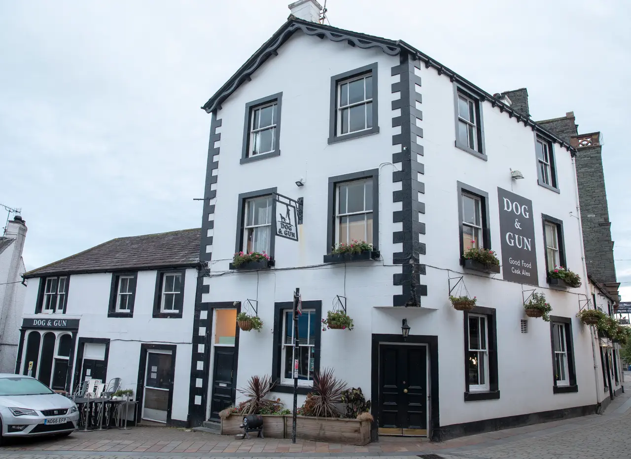 The white-painted Dog and Gun pub on Lake Road in Keswick, with hanging baskets and its sign above the door