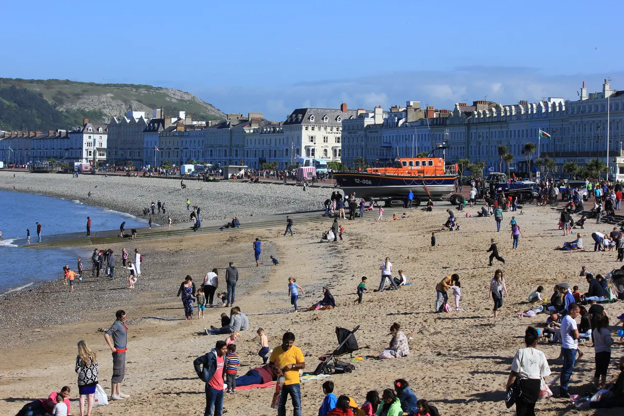 The North Shore on a sunny day, with families on the sand, the lifeboat on the beach and the row of white seafront hotels under the Great Orme