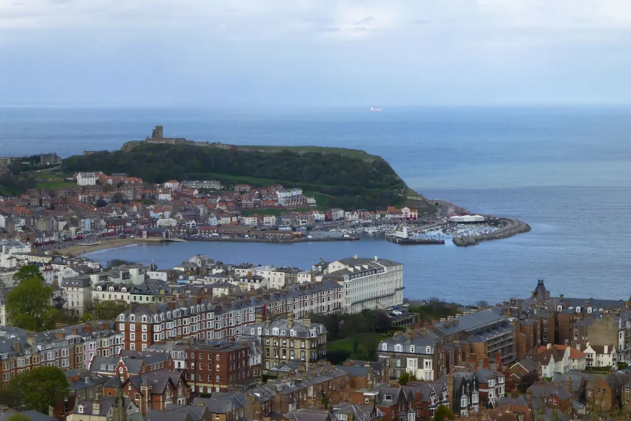 Scarborough from above: the South Cliff's terraces in front, the harbour full of boats, and the castle on its green headland over the sea