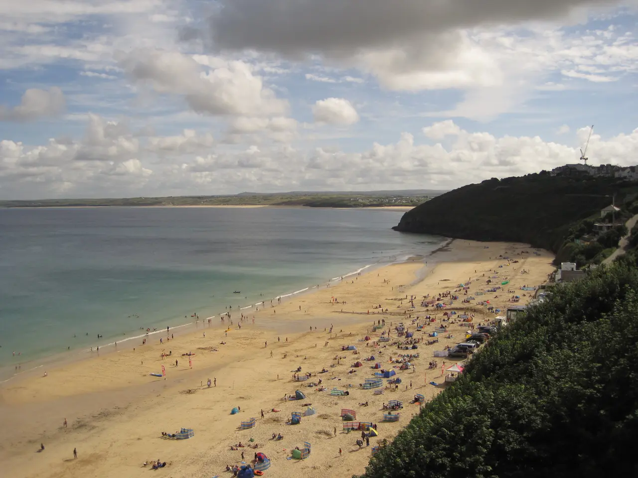 The long sandy beach at Carbis Bay seen from the cliff path on a busy summer day, with the bay curving away to the dunes beyond