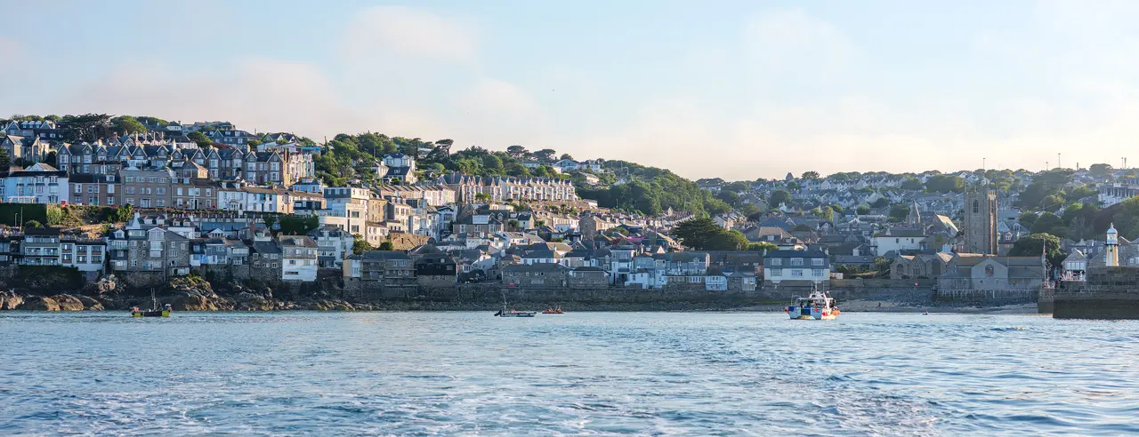 Grey and white houses climbing the hill above St Ives harbour, seen from the sea in soft morning light