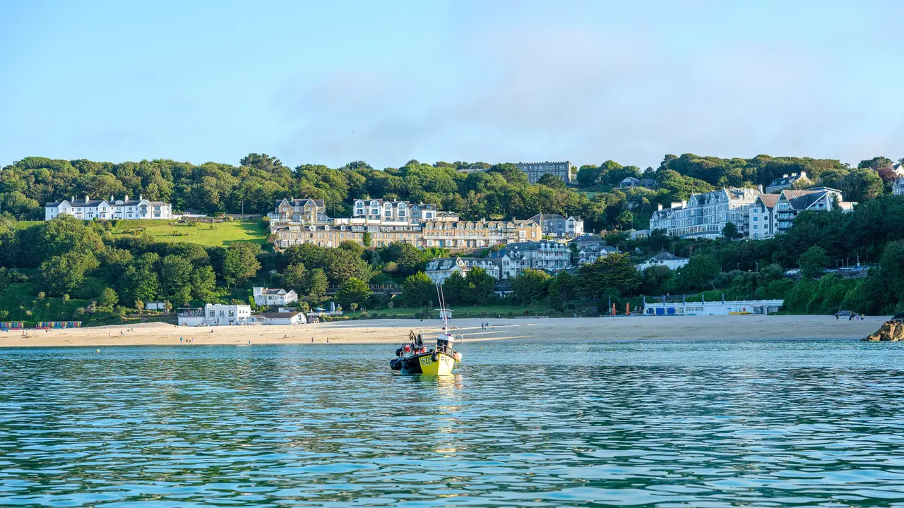 Porthminster Beach seen from the water, with a fishing boat in the foreground and white hotels among the trees on the hill above