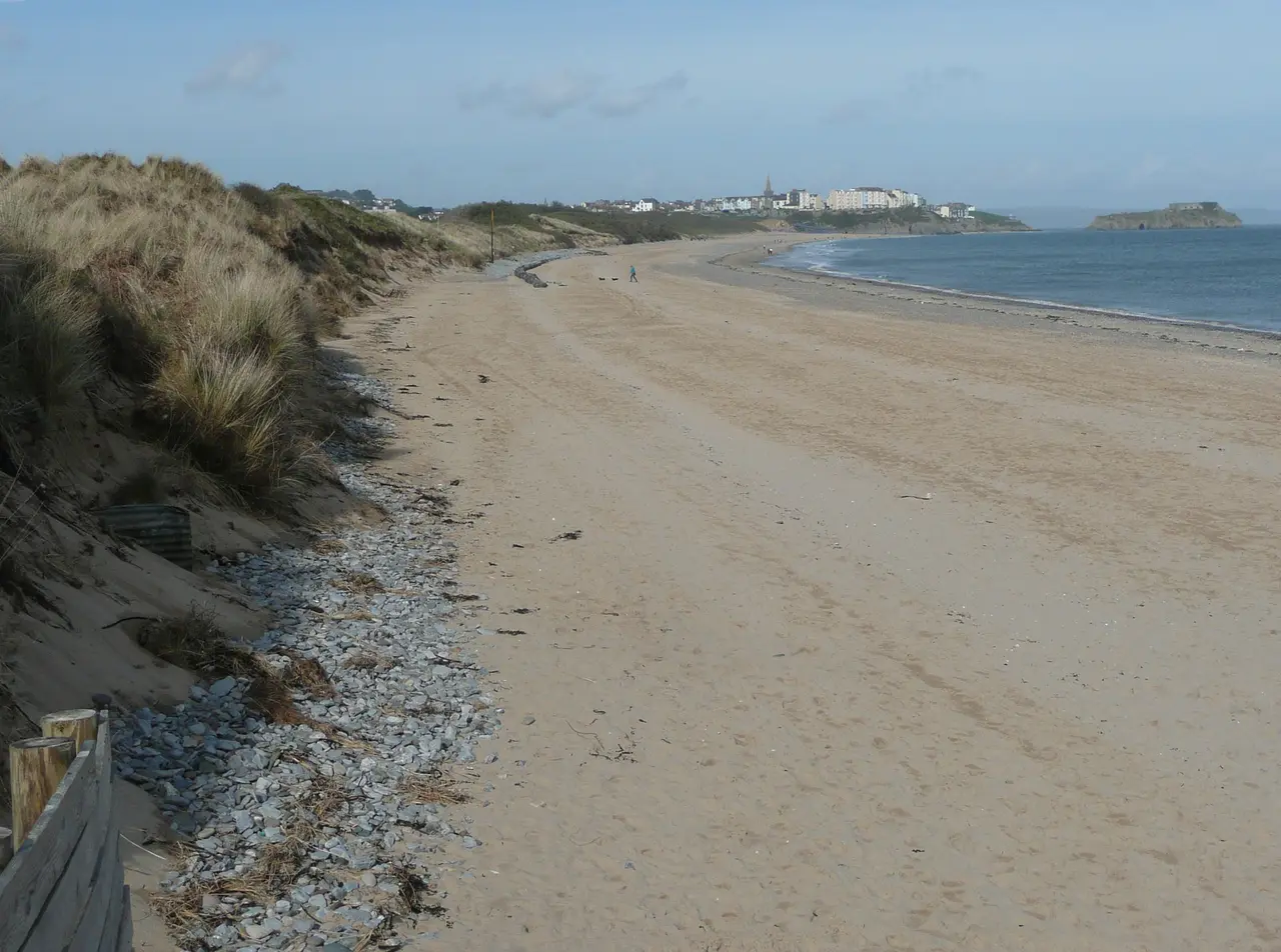 A long empty stretch of South Beach below marram-covered dunes, with Tenby and St Catherine's Island in the distance