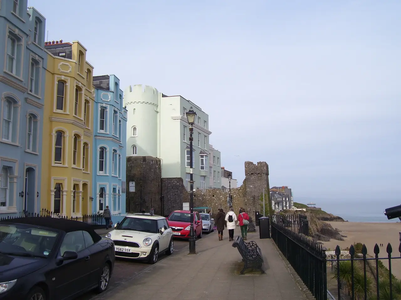 Blue, yellow and white Georgian houses along the Esplanade, with people walking by the railings and the old town wall