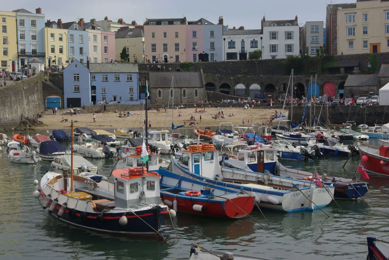 Red, blue and white fishing boats moored in Tenby harbour below a row of pastel-coloured houses