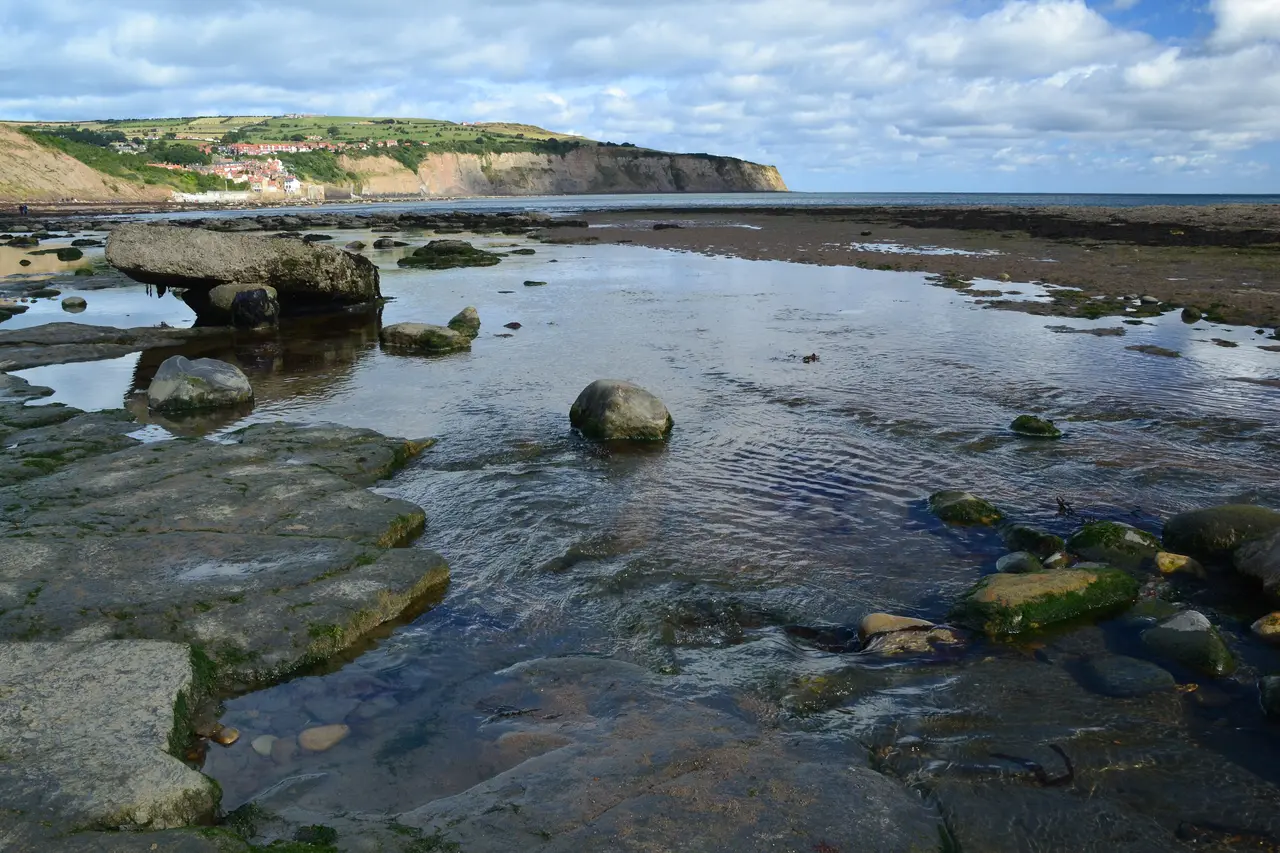 Rock pools and flat rock ledges on the shore at Robin Hood's Bay at low tide, with the village and the far headland across the bay