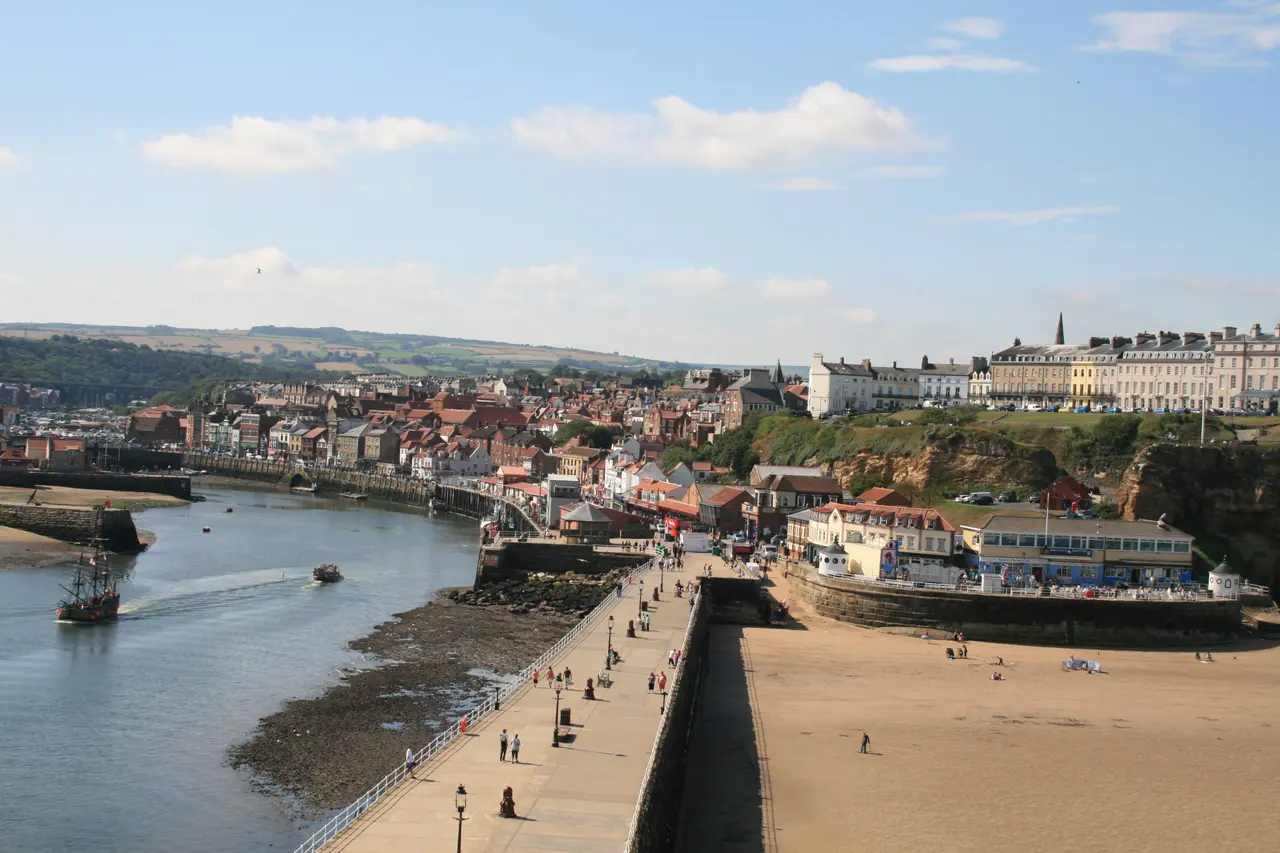 Whitby's West Cliff from the harbour: tall terraced houses along the clifftop above the beach and the pier