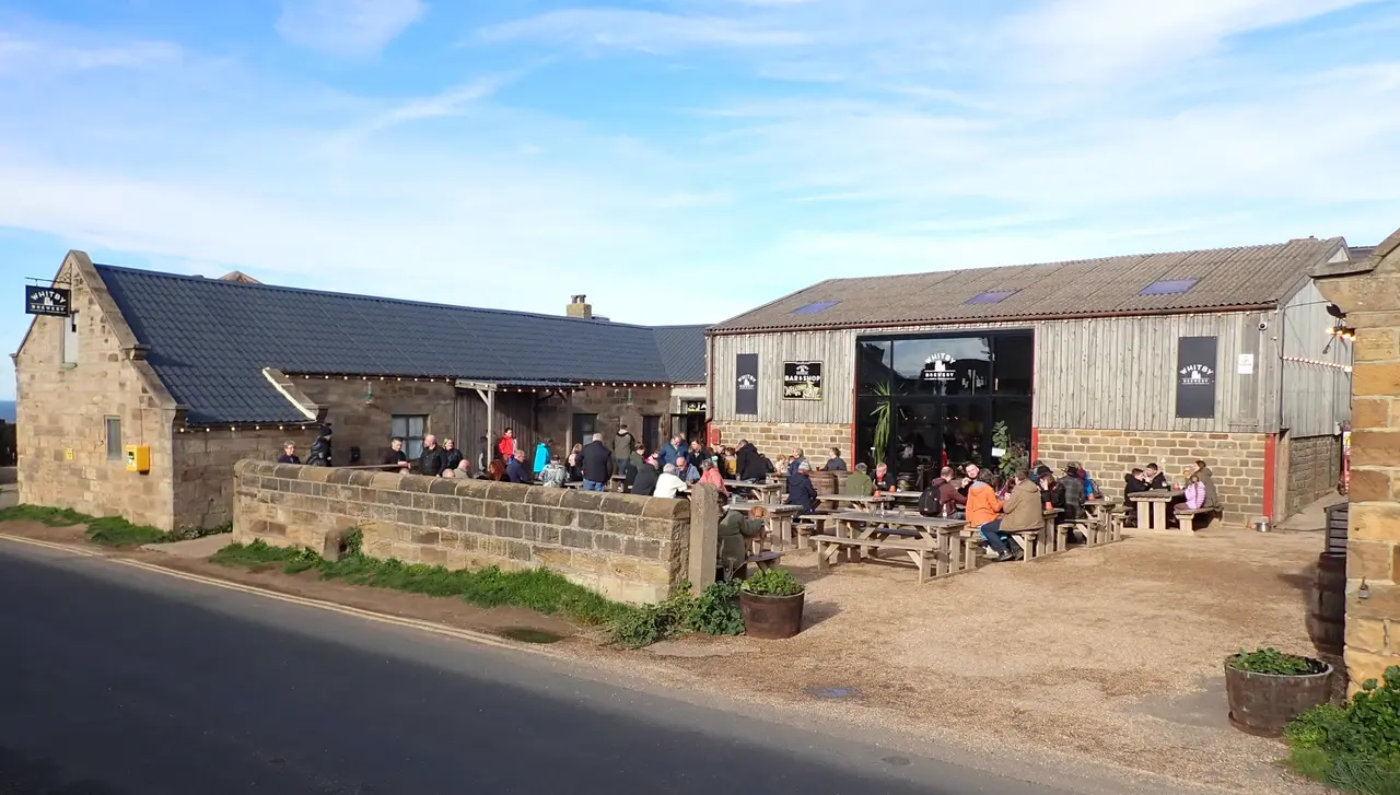 Whitby Brewery's stone and timber buildings on Abbey Lane, with people at picnic tables in the yard outside